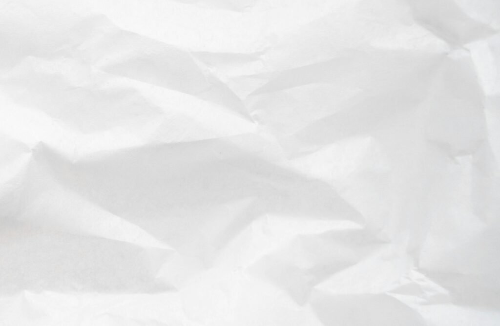 A detailed texture of crumpled white paper with visible folds and creases.